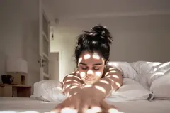 Vrouw in de slaapkamer bij bijna gesloten rolluiken met een mooi lichtspel