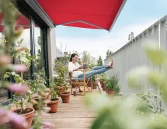 Frau sitzt unter roter Markise auf Balkon