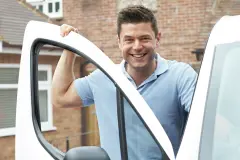 Servicetechniker steht an einem Einsatzfahrzeug vor einem Wohngebäude, bereit für Montage oder Wartung von Alu Rolladen