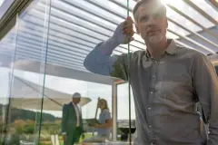Mann bewegt Glasschiebetür an Lamellendach in Ausstellung